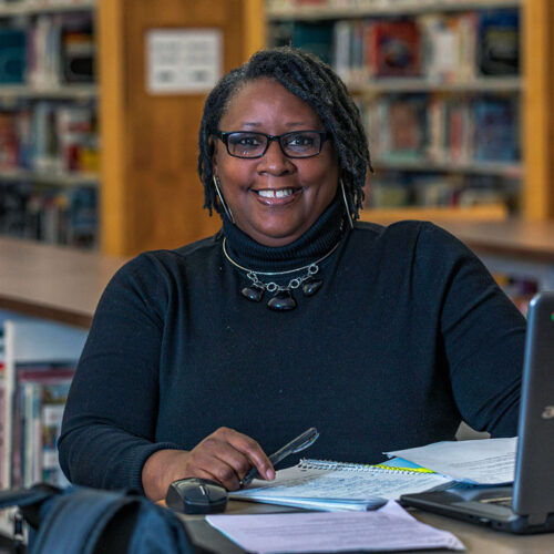 Adult-Student-Sitting-at-Desk-Smiling-at-Camera-Featured